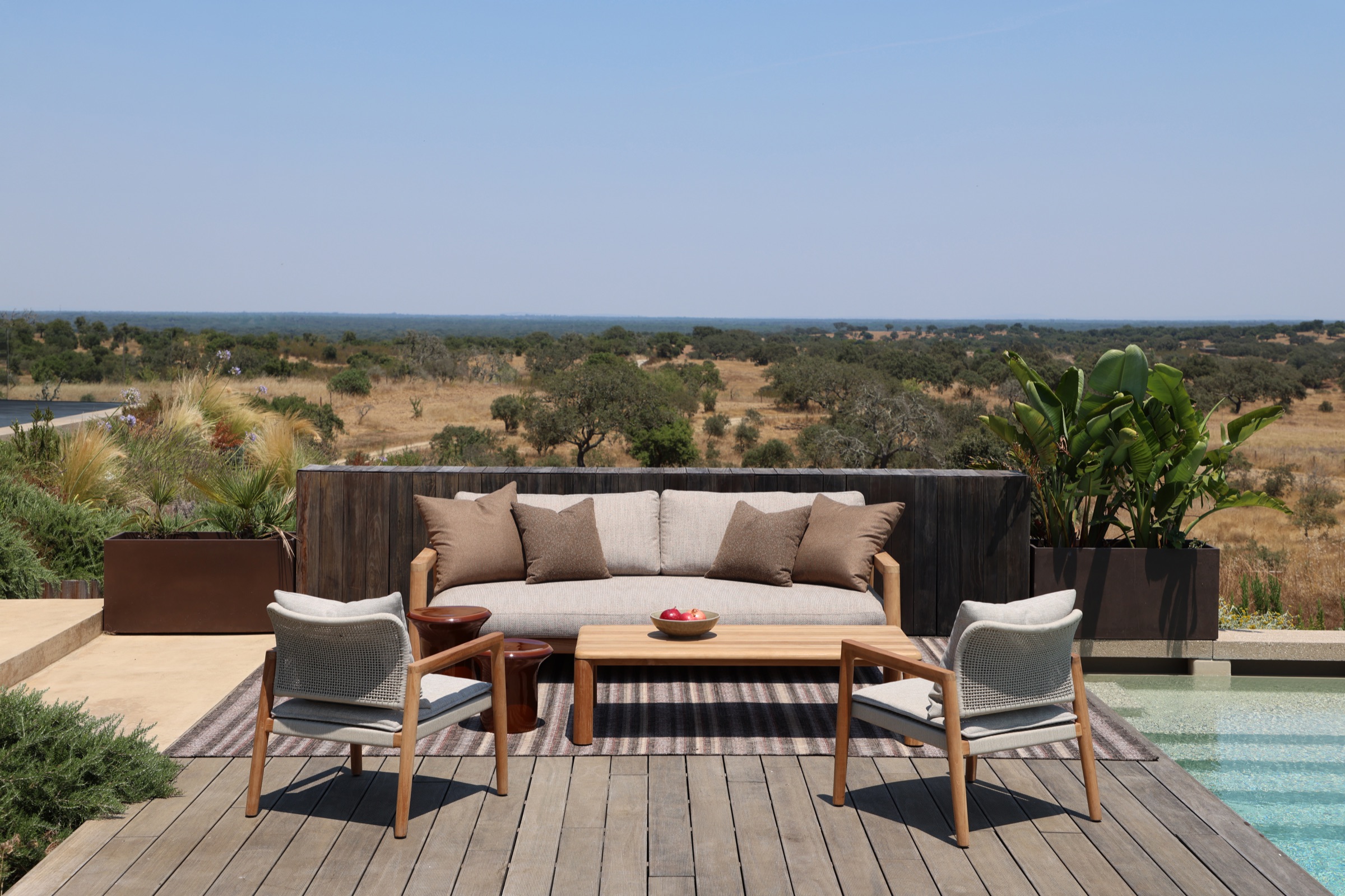 Outdoor sofa, lounge chairs and teak coffee table on a deck by a pool